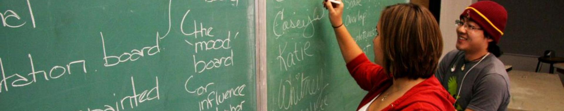 Student watches while TA writes on a chalkboard. 