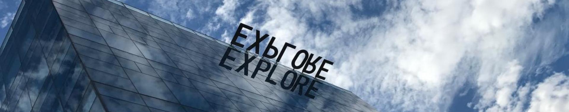 ASU' Tempe campus Coor building windows relecting the "Explore" sign and blue skys with white clouds. 