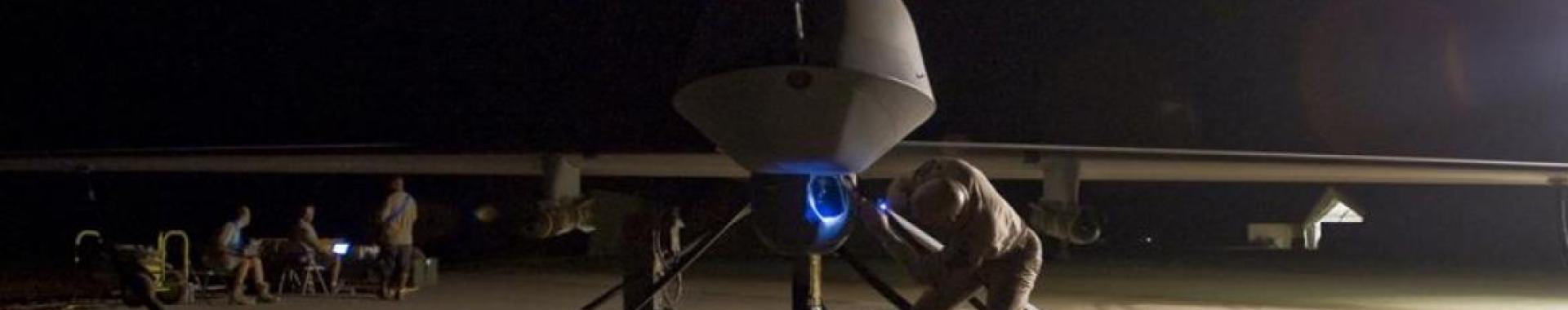 Military drone on the ground being serviced at night.